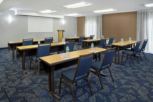 Un salón de conferencias con mesas, sillas y una pantalla para proyector.