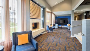 A hotel lobby with a seating area, a fireplace, and a television screen. - Courtyard by Marriott Southfield (Southfield)