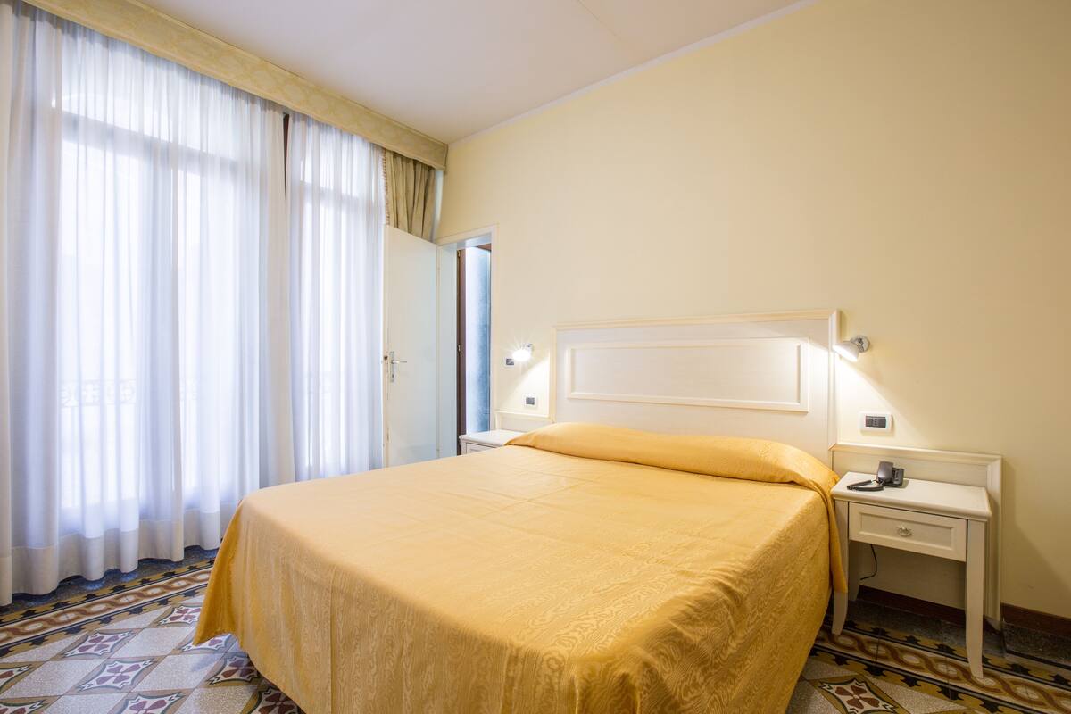 Una camera d'albergo con un letto, un comodino e un tavolino di fianco al letto.