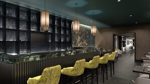 A modern bar area with a glass counter, patterned yellow chairs, and pendant lighting. - Universo And Nord Hotel (Venice)