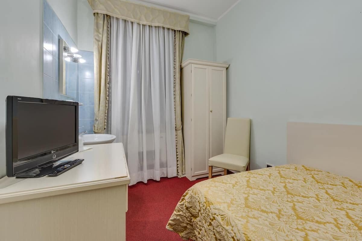 Camera d'albergo con un letto, una TV su una scrivania, un armadio e un bagno con uno specchio e tende.