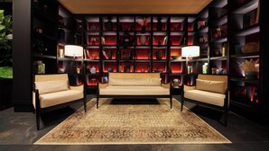 A room with a sofa, two armchairs, a patterned rug, and a bookshelf filled with various decorative items. - Universo And Nord Hotel (Venice)