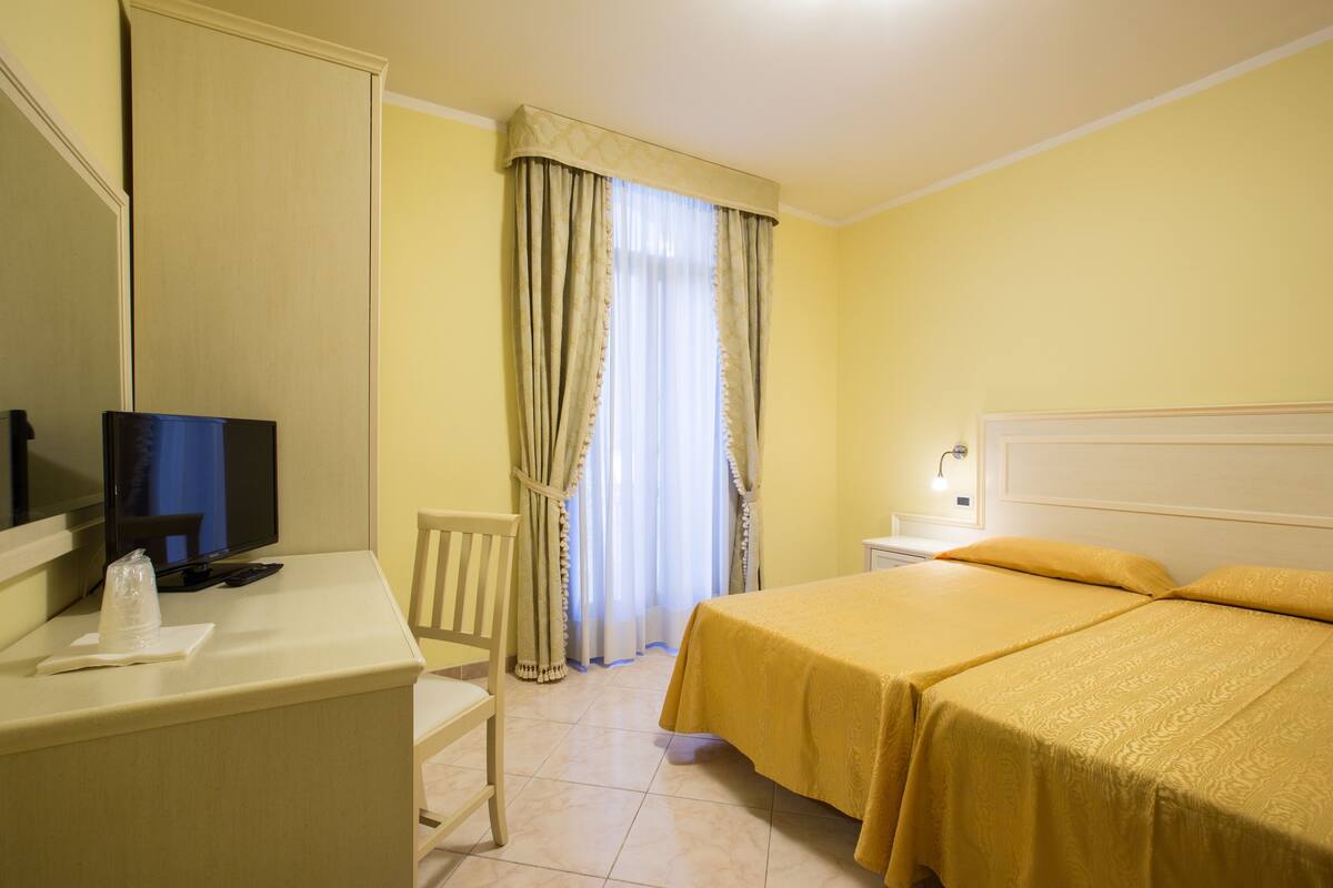 Una camera d'albergo con un letto, una scrivania con un computer, una sedia e un televisore.
