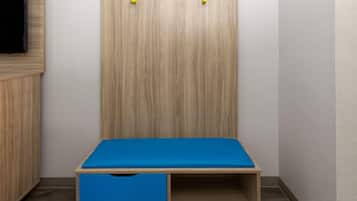 A corner room with a wooden wardrobe, a blue table, and a TV mounted on the wall.