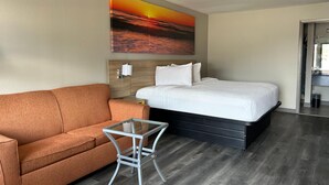 A hotel room with a bed, a sofa, a small table, and a painting on the wall. - Days Inn by Wyndham Natchitoches (Natchitoches)