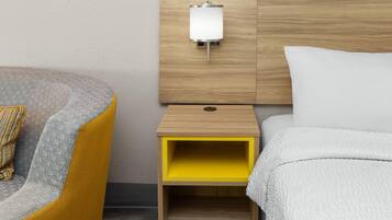 Una habitación de hotel con una cama, una mesita de noche con lámpara, una silla y un pequeño armario amarillo.