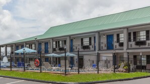 A motel with a green roof, multiple balconies, and a swimming pool area with umbrellas. - Days Inn by Wyndham Natchitoches (Natchitoches)