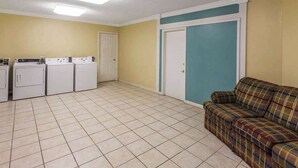 A laundry room with four washing machines, a door, and a couch. - Days Inn by Wyndham Natchitoches (Natchitoches)