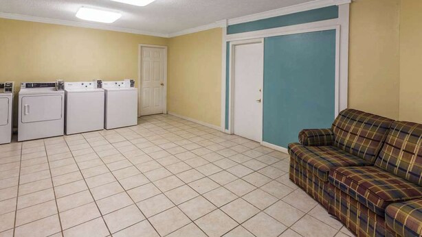 A laundry room with four washing machines, a door, and a couch. - Days Inn by Wyndham Natchitoches (Natchitoches)