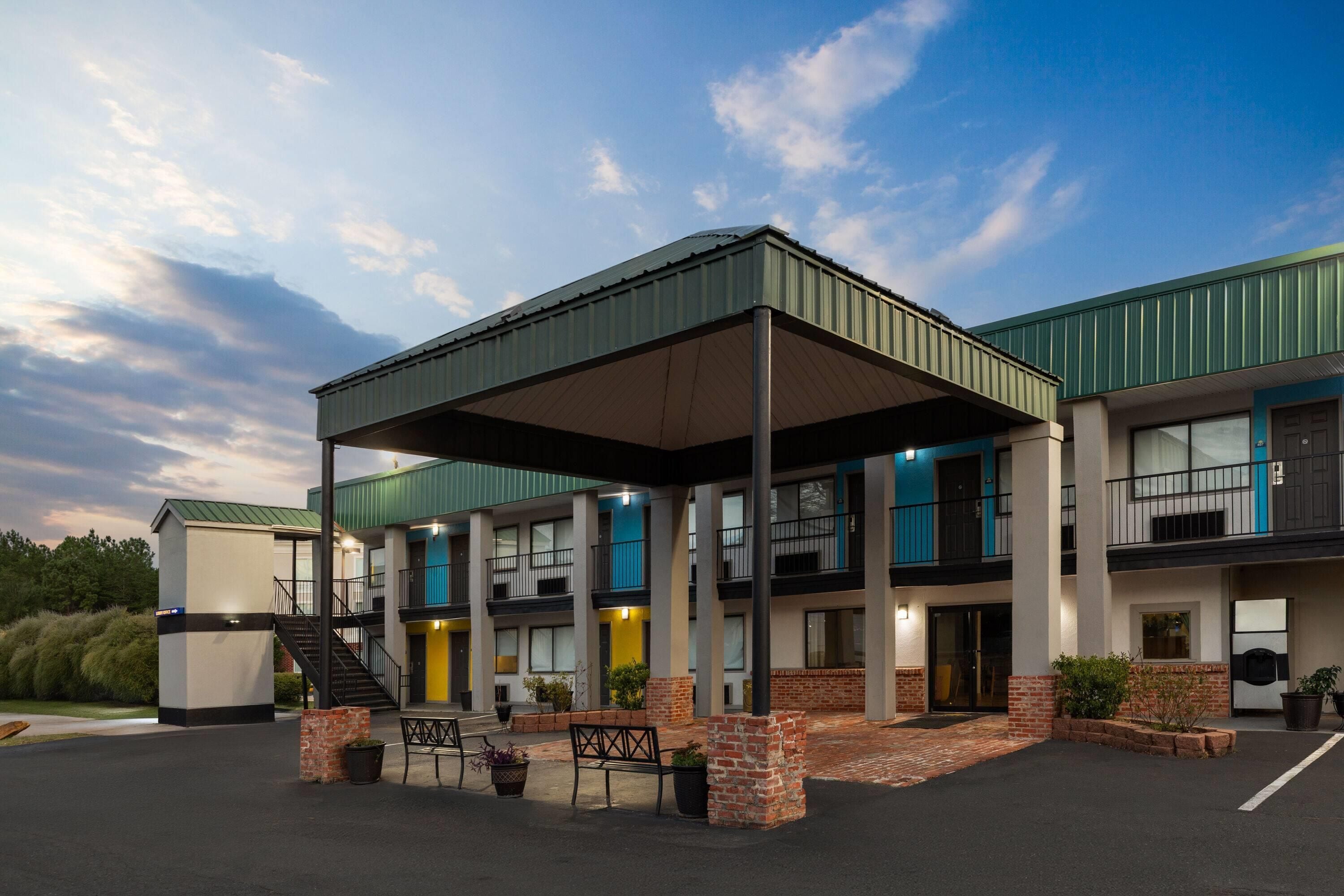 A multi-story hotel with a covered outdoor area, multiple balconies, and a parking lot.