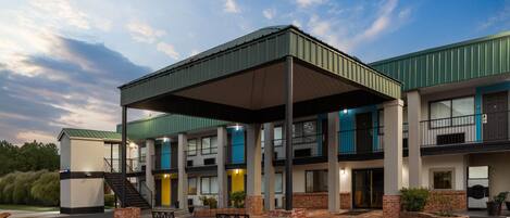 A multi-story hotel with a covered outdoor area, multiple balconies, and a parking lot.