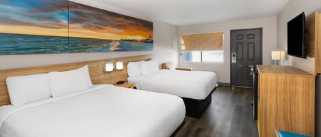 Habitación de hotel con dos camas, televisión, escritorio y un cuadro con atardecer sobre el océano.