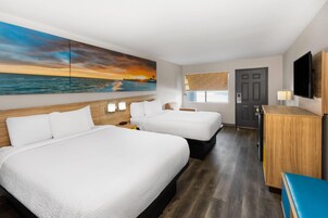 A hotel room with two beds, a TV, a desk, and a painting of a sunset over the ocean.