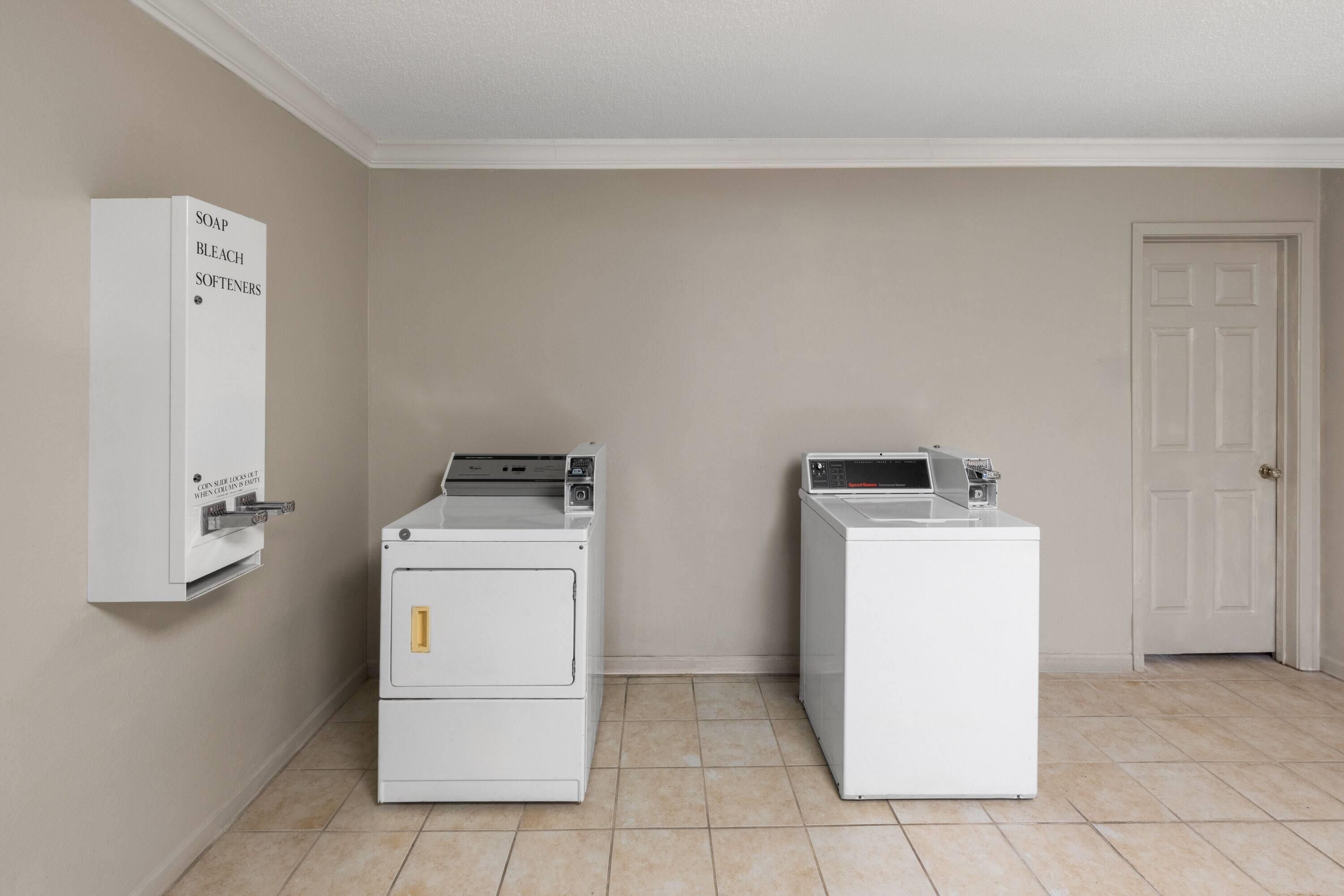 A laundry room with two stacked washer and dryer units, a coin-operated soap dispenser, and a white door.