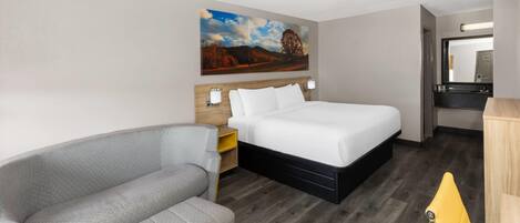 A hotel room with a bed, a sofa, a nightstand, a lamp, a painting, and a mirror.