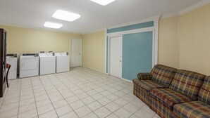 A laundry room with four white washing machines, a door, and a blue wall. - Days Inn by Wyndham Natchitoches (Natchitoches)