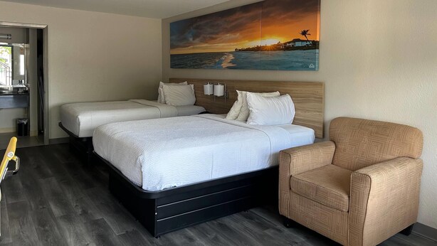 A hotel room with a large bed, two bedside tables, a chair, and a painting of a sunset over the ocean. - Days Inn by Wyndham Natchitoches (Natchitoches)
