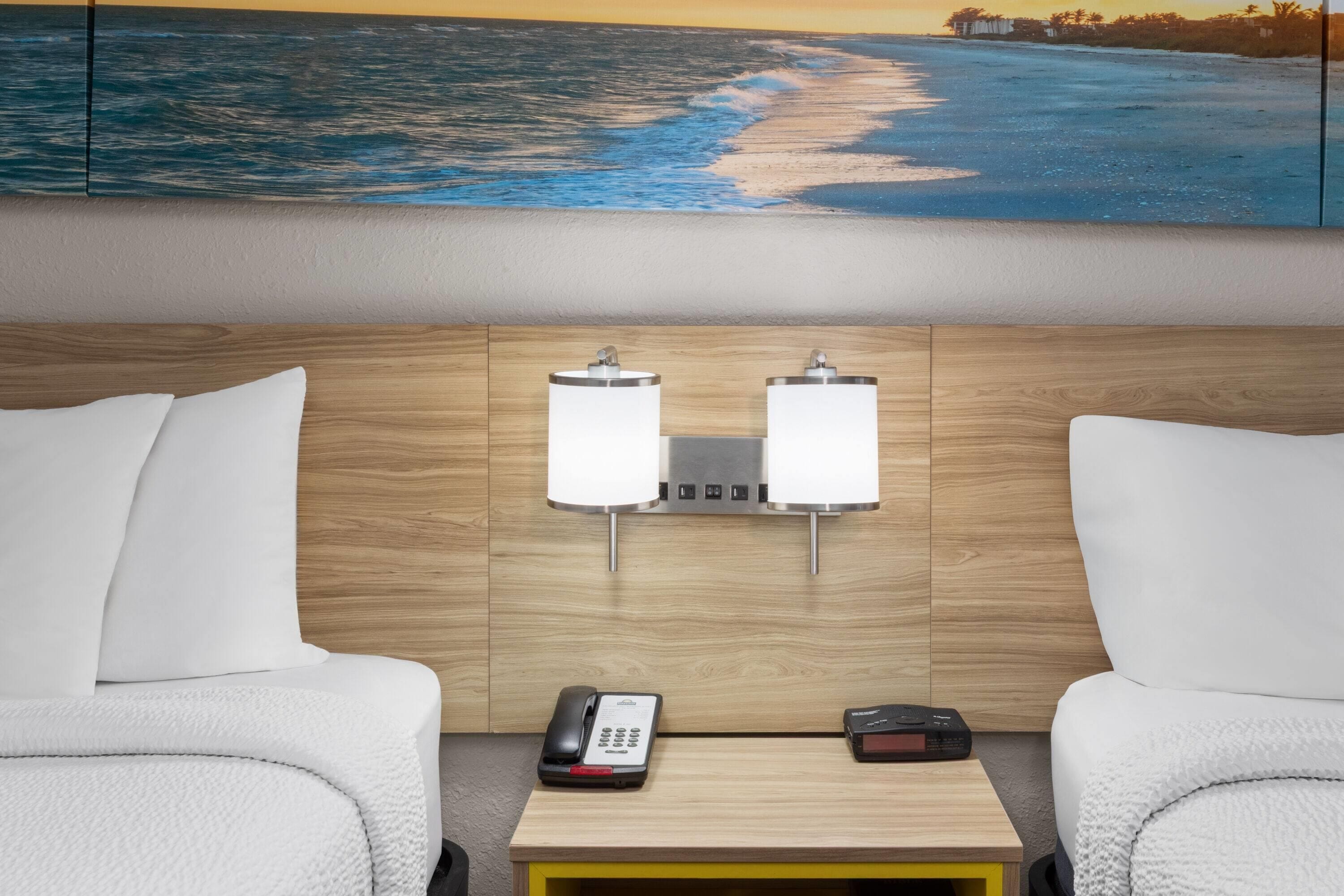 A hotel room with a wooden headboard, two bedside lamps, a telephone, and a small table.