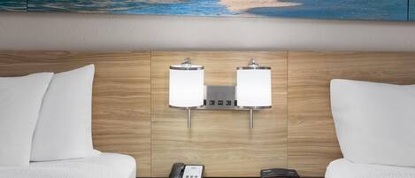 A hotel room with a wooden headboard, two bedside lamps, a telephone, and a small table.
