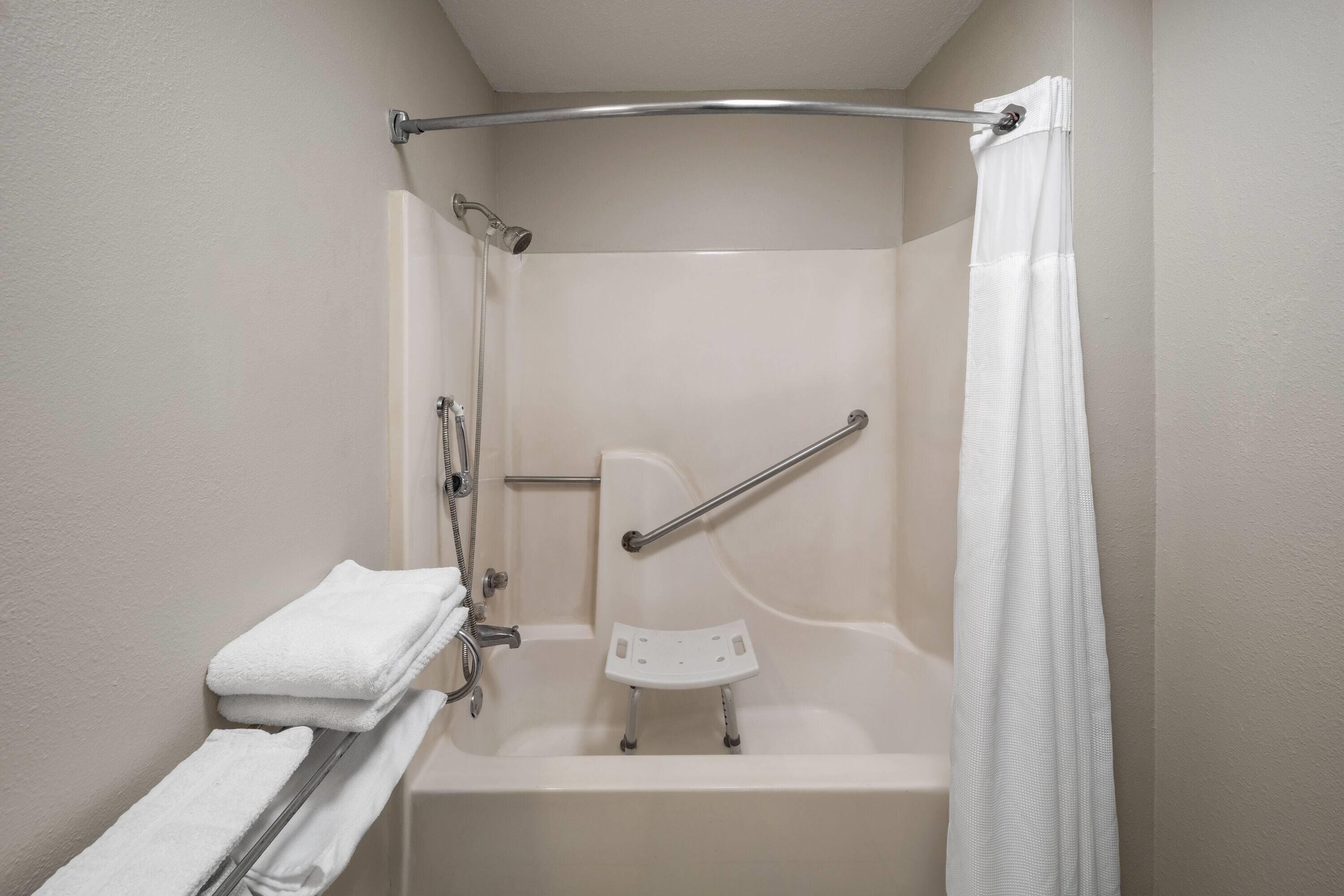 A walk-in shower with a grab bar, a white towel on a rack, and a shower curtain.
