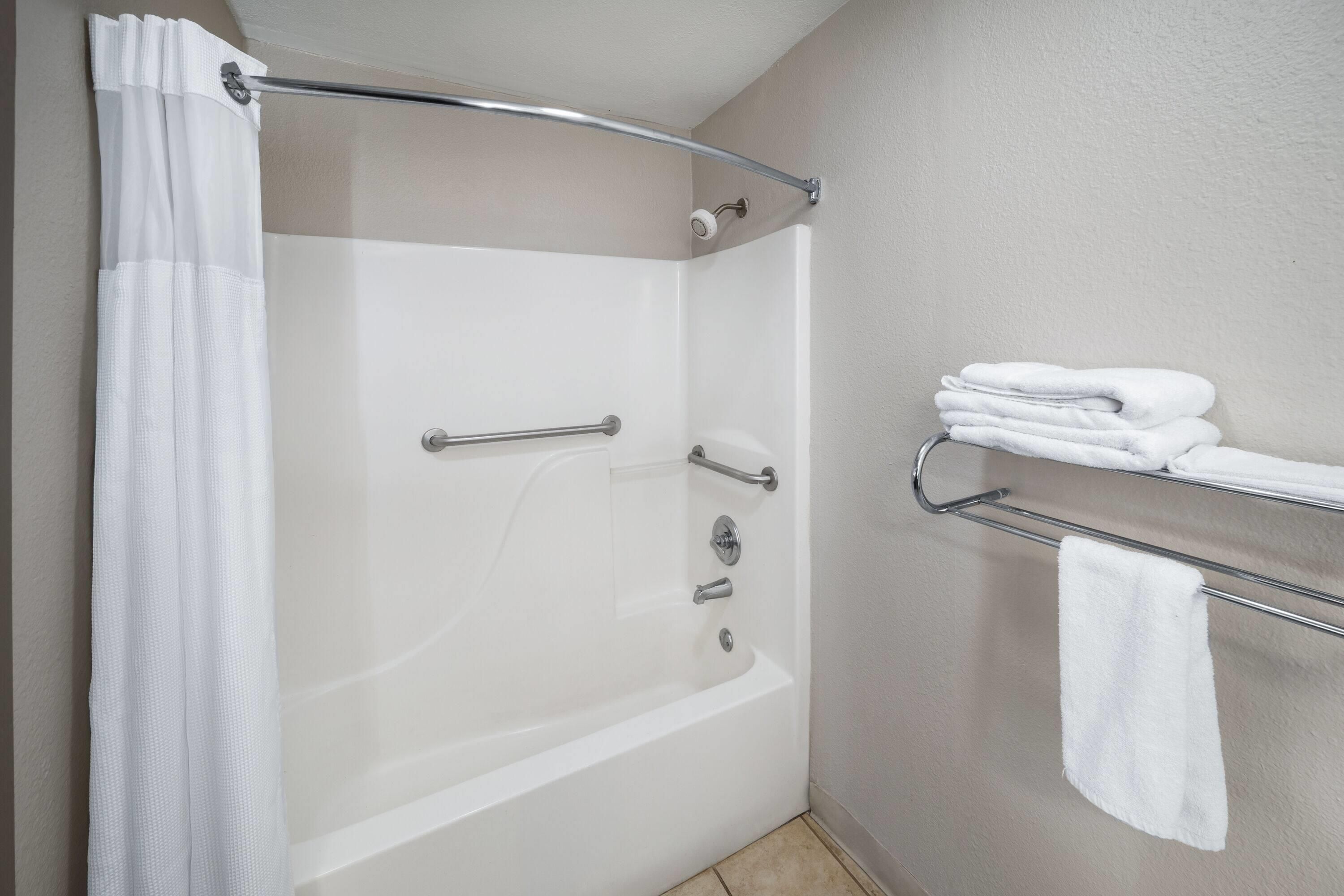 A bathroom with a bathtub, a shower curtain, and a towel rack with folded towels.