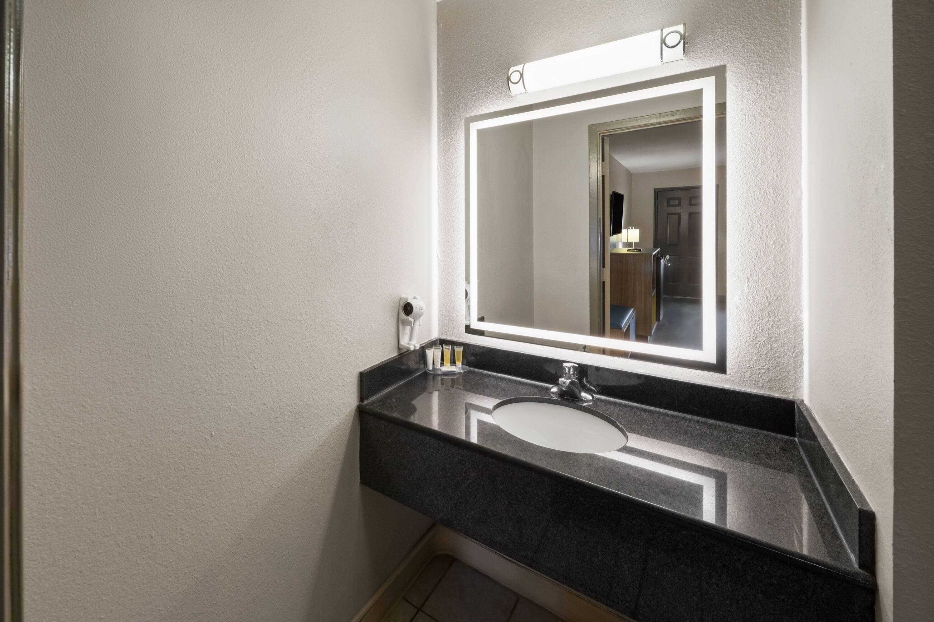 A bathroom with a black countertop, a sink, a mirror, and a hairdryer.
