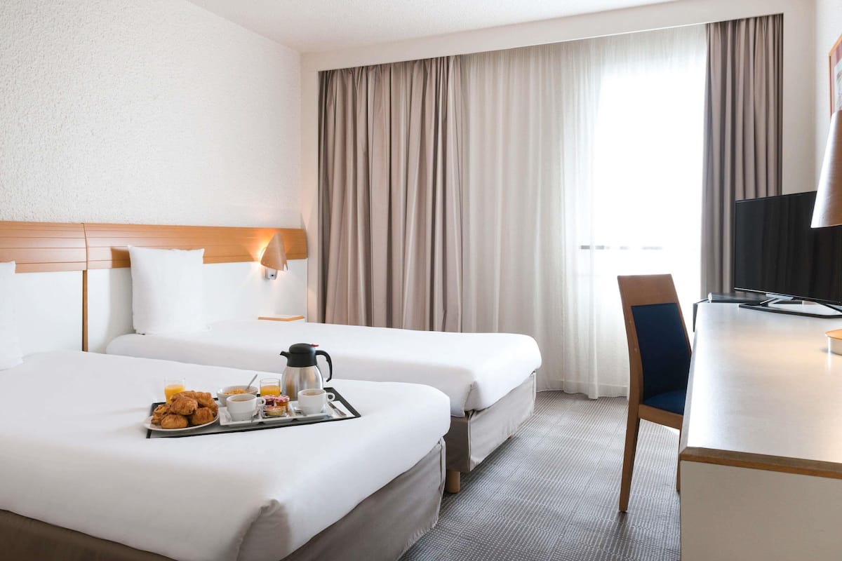 Habitación de hotel con dos camas, un escritorio con televisor y una bandeja de desayuno sobre la cama de la izquierda.