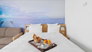 Une chambre d’hôtel avec un lit, un plateau de petit-déjeuner, une tête de lit en bois et une fresque murale représentant une jetée et l’eau.