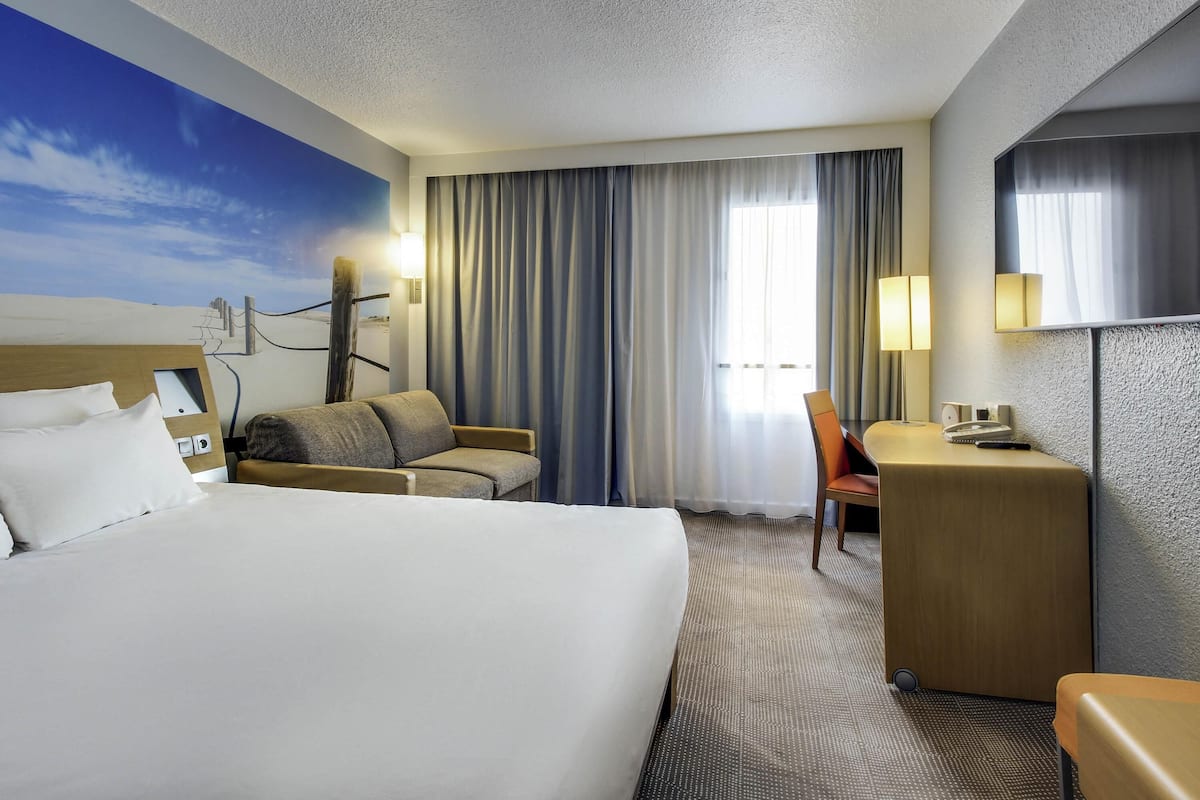 Habitación de hotel con una cama grande, un escritorio, una silla y vista al cielo a través de la ventana.