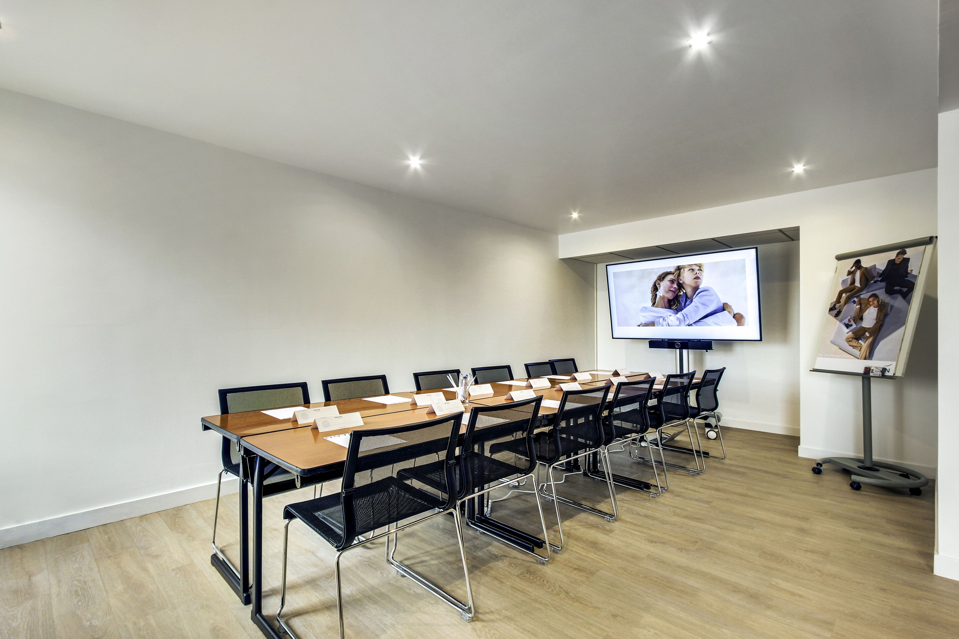 A conference room with a long table, black chairs, a projector screen, and a whiteboard.