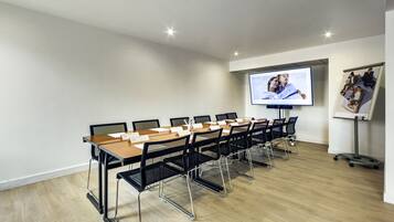 A conference room with a long table, black chairs, a projector screen, and a whiteboard.