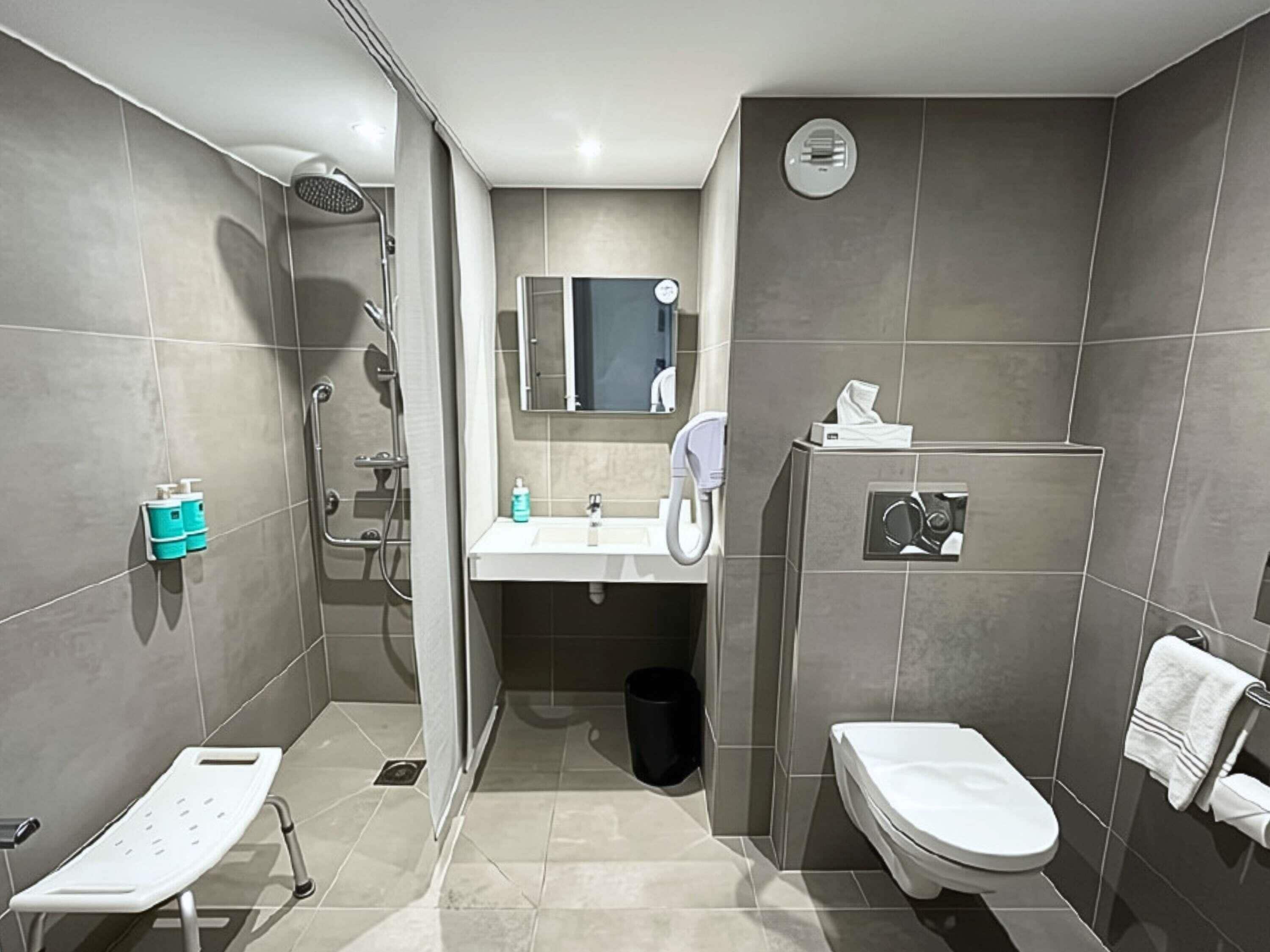 Een moderne badkamer met douche, toilet, wastafel en spiegel.
