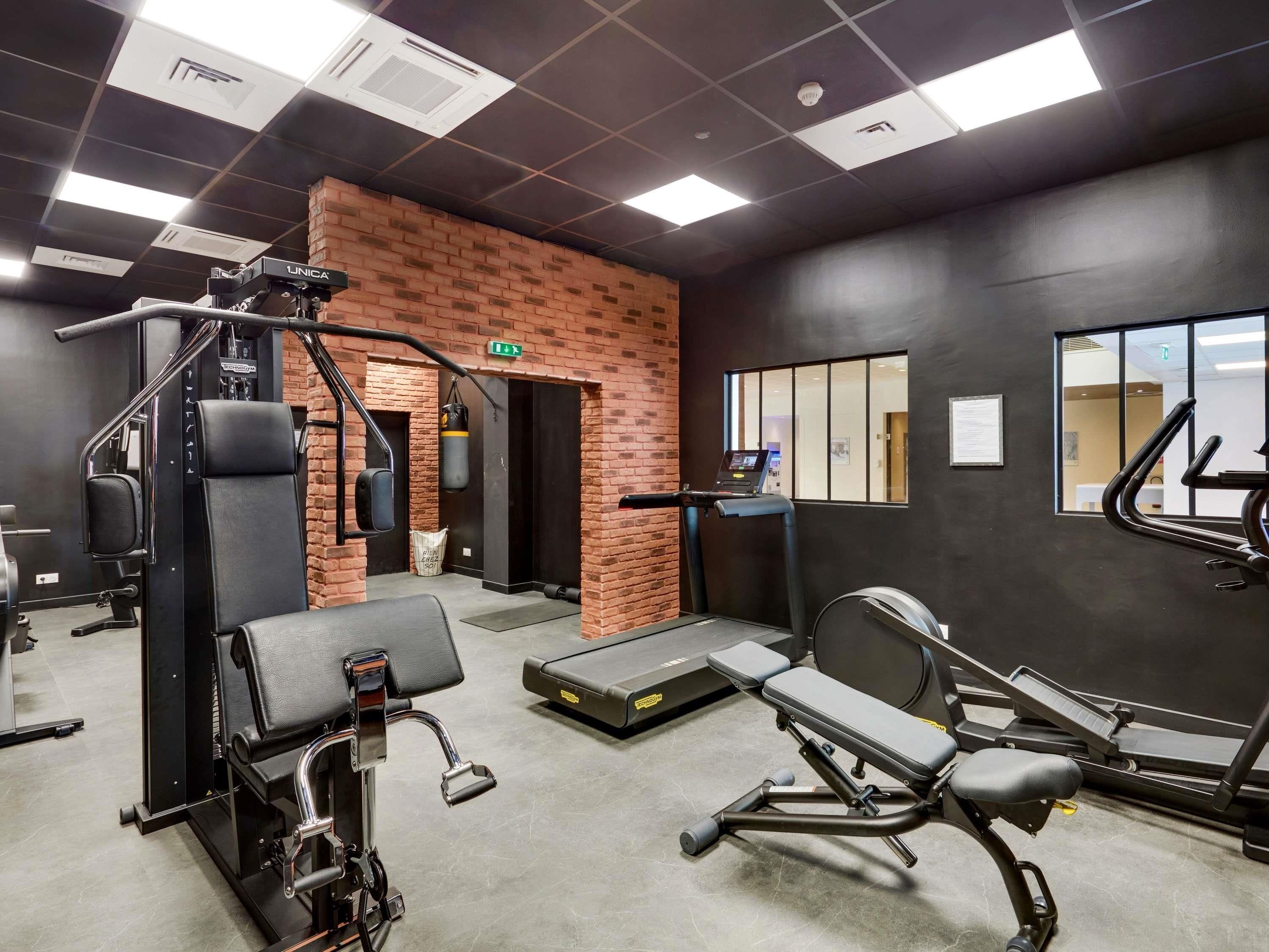 A gym with exercise equipment, a brick wall, and a window.