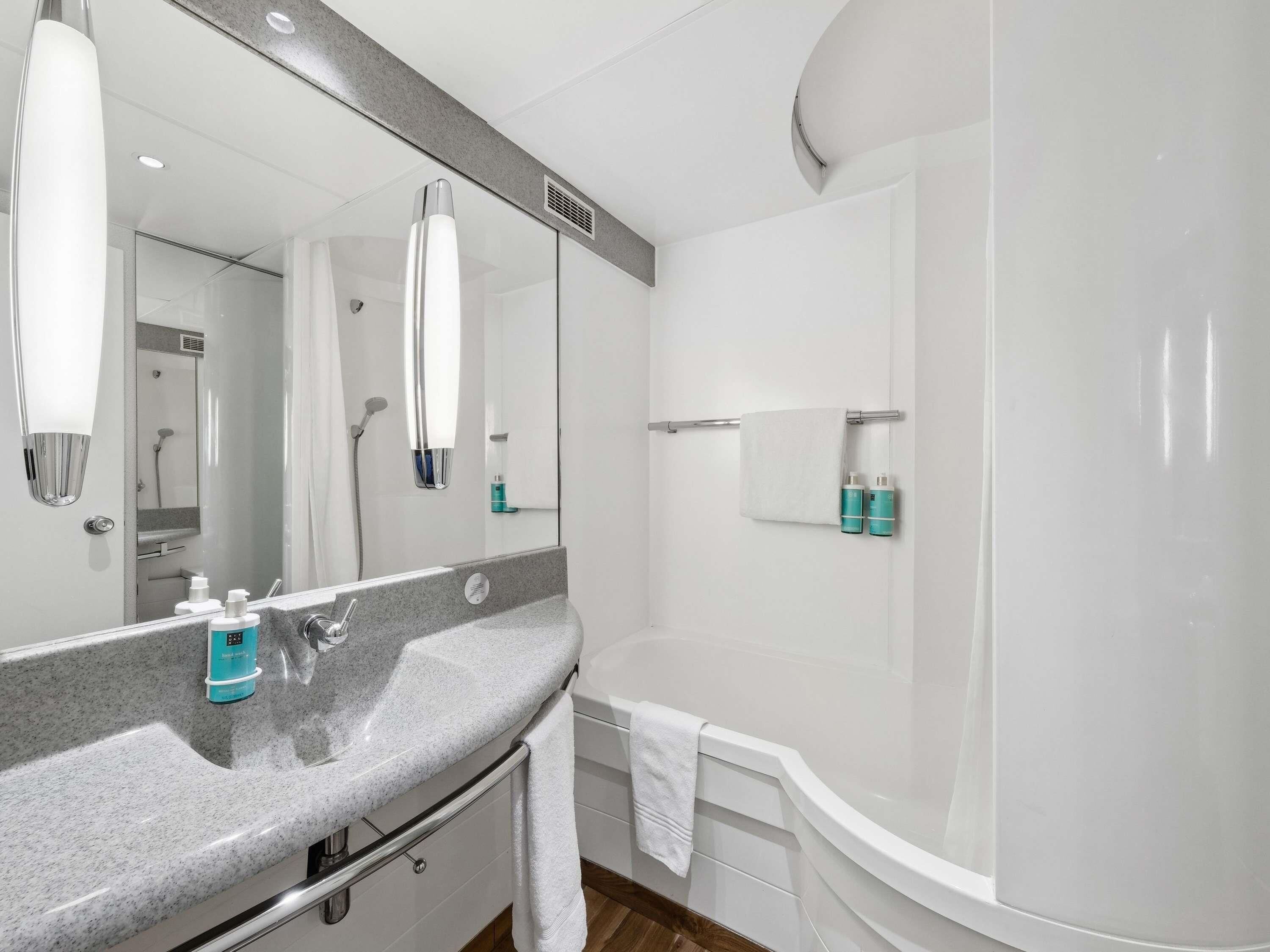 Une salle de bain moderne avec un comptoir en granit, un grand miroir, une baignoire et un espace douche.