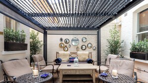 An outdoor patio with a wooden table and chairs, a pergola overhead, and decorative mirrors on the wall. - Dukes London (London)