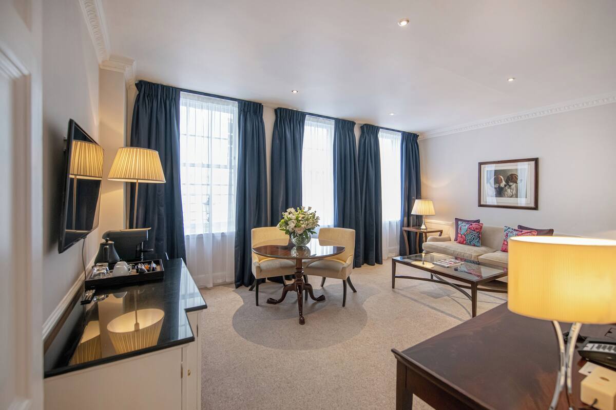 Une chambre d’hôtel équipée d’une table à manger, de deux chaises, d’un canapé, d’une table basse, d’un téléviseur et d’une lampe.