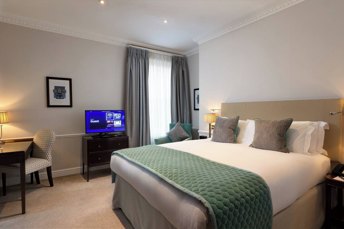 Une chambre d’hôtel avec un lit, un bureau, une télévision et une fenêtre avec des rideaux.