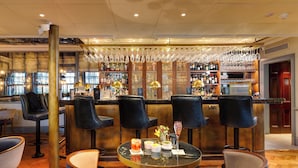 A bar area with high stools, a round table with drinks, and a bar stocked with bottles and glasses. - Dukes London (London)