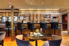 A bar area with high stools, a round table with a drink, and a bar stocked with bottles and glasses. - Dukes London (London)