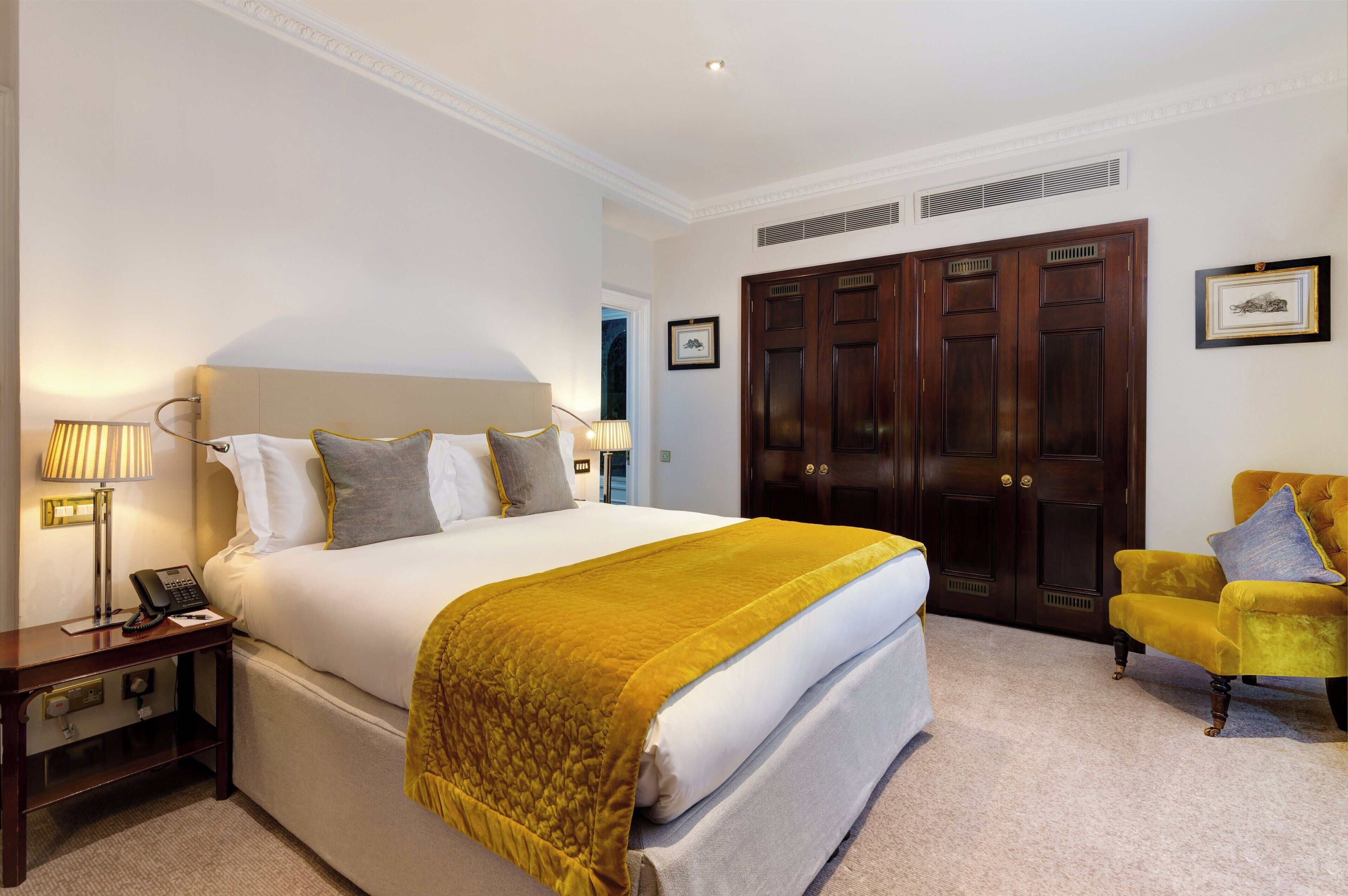A hotel room with a large bed, a bedside table with a lamp, a chair, and a wardrobe.