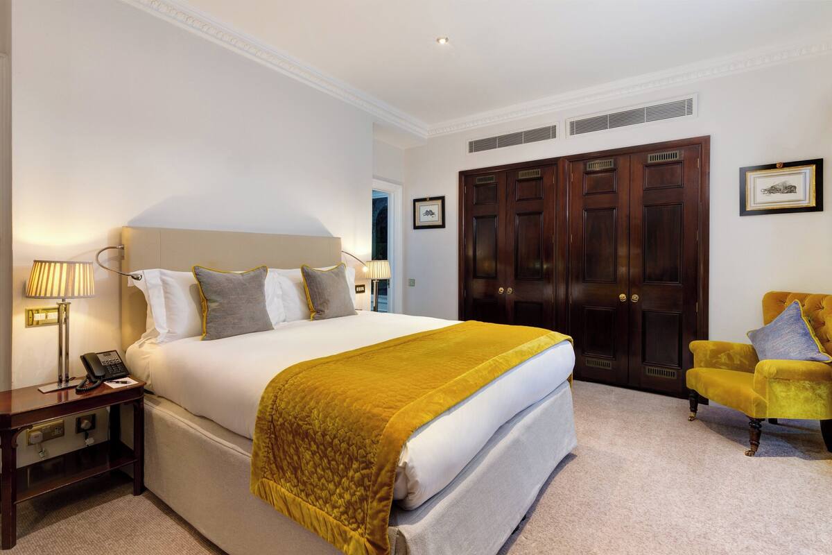 Une chambre d’hôtel avec un grand lit, une table de chevet avec une lampe, une chaise et une armoire.