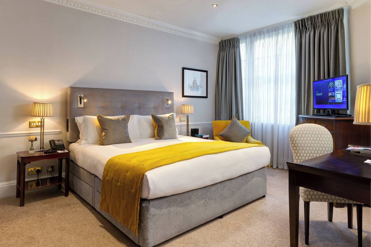Une chambre d’hôtel avec un grand lit, un bureau, une chaise, une télévision et un tableau encadré au mur.
