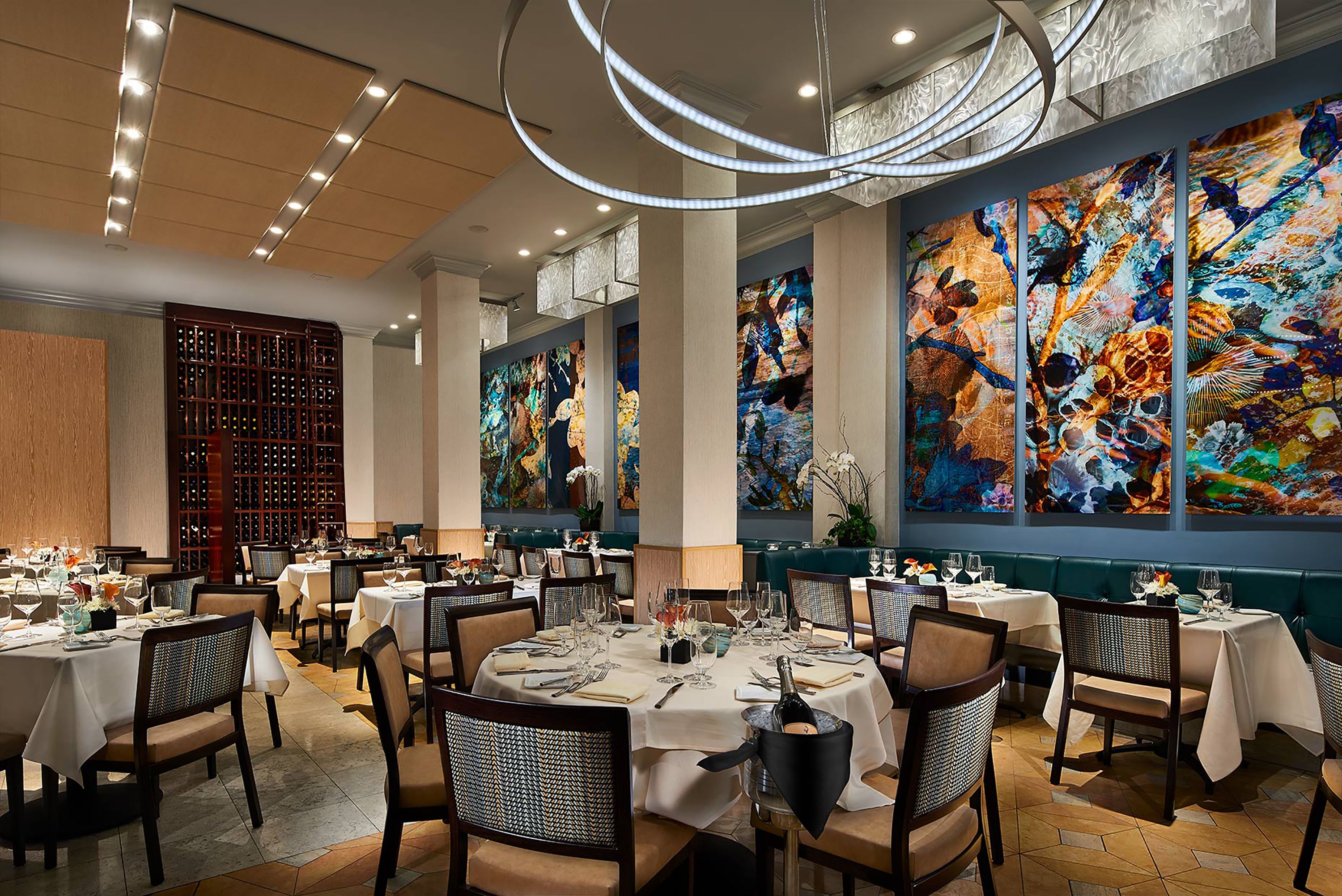 A restaurant with round tables, chairs, and large abstract paintings on the walls.