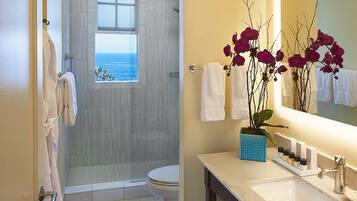 A bathroom with a large mirror, white sink, and a shower with a view of the ocean.