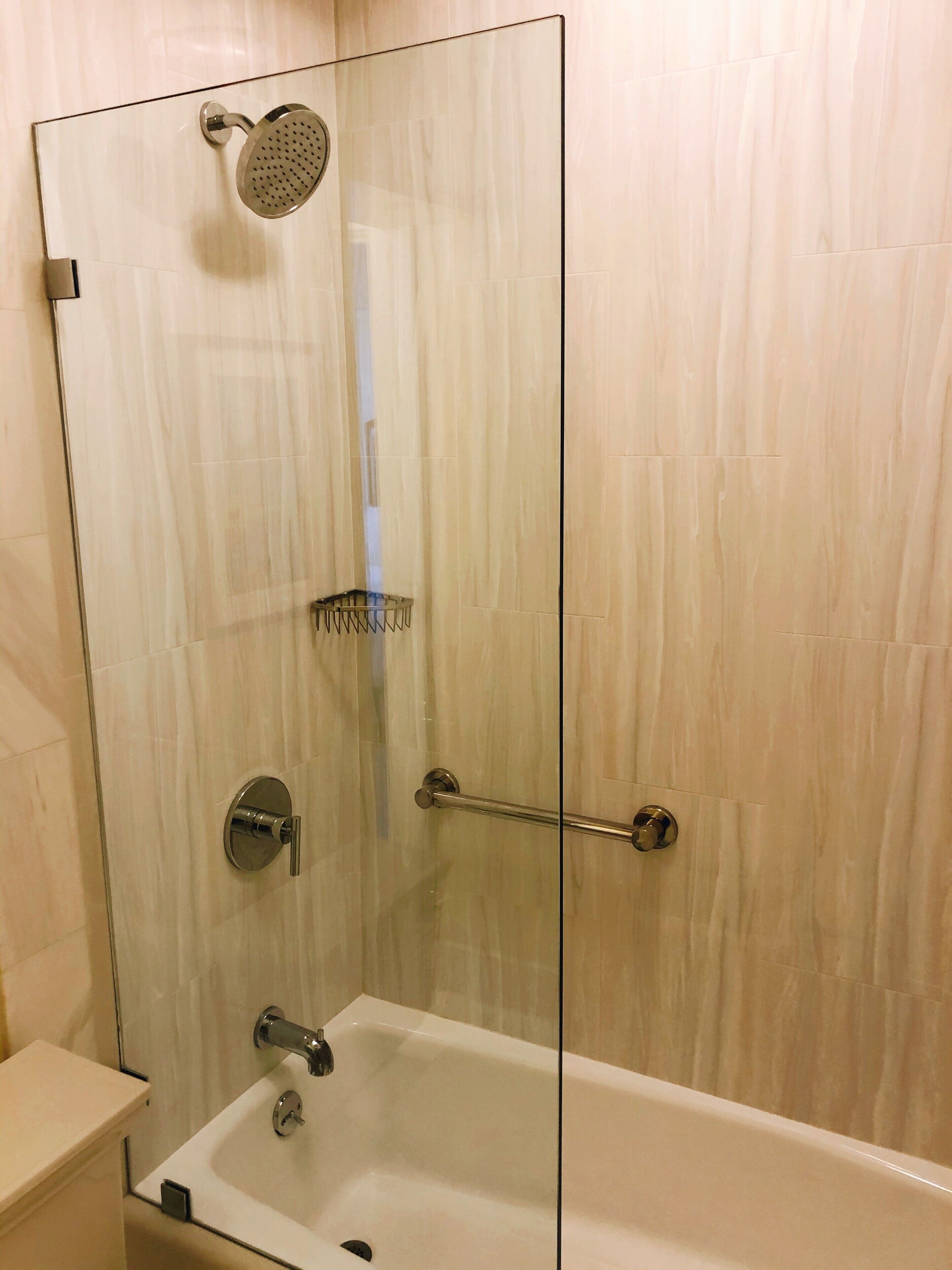 A glass-enclosed shower with a handheld showerhead, a handheld showerhead, and a handheld showerhead.