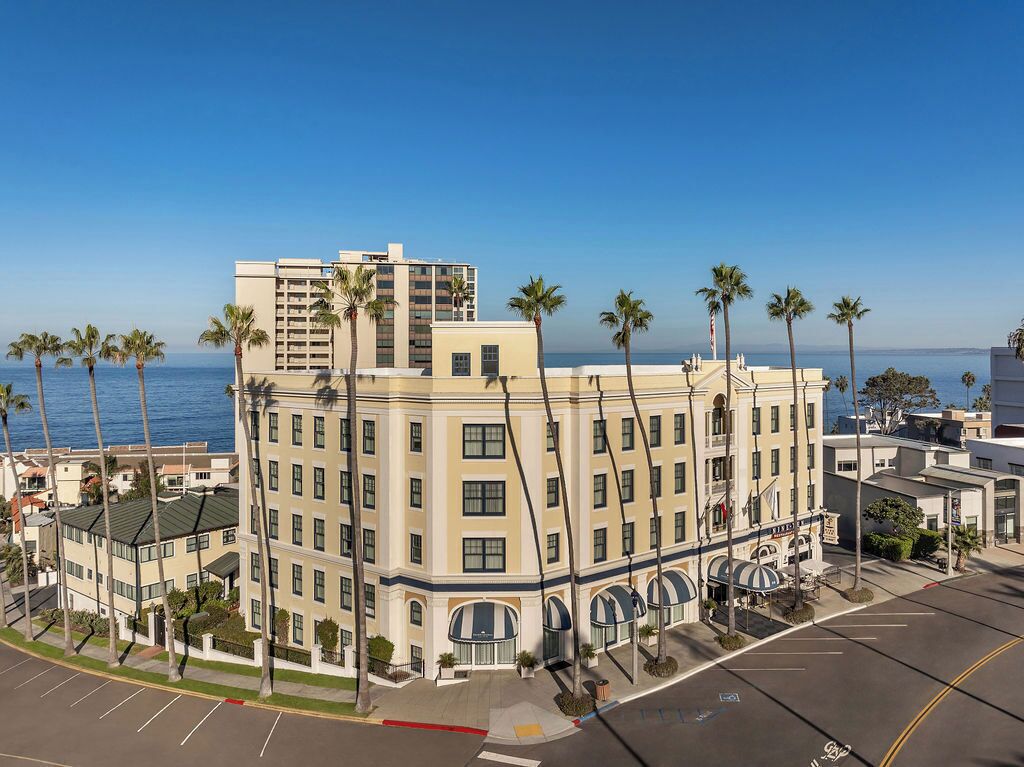 A multi-story hotel with a central courtyard, palm trees, and a view of the ocean.