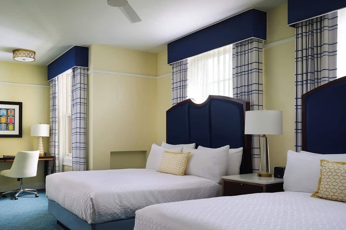A hotel room with two beds, a desk, a chair, and a window with curtains.
