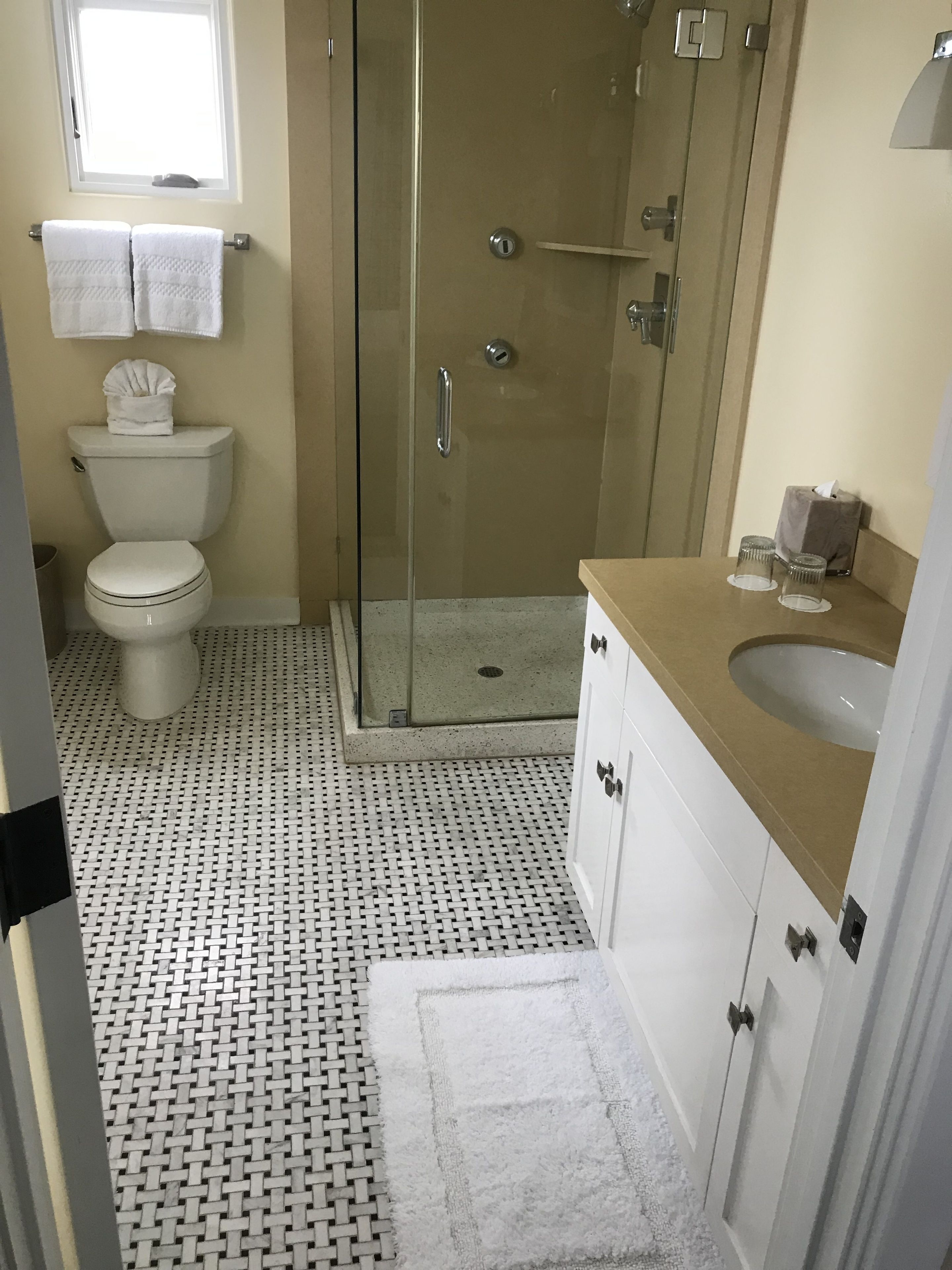 A bathroom with a toilet, shower, sink, and a small window.