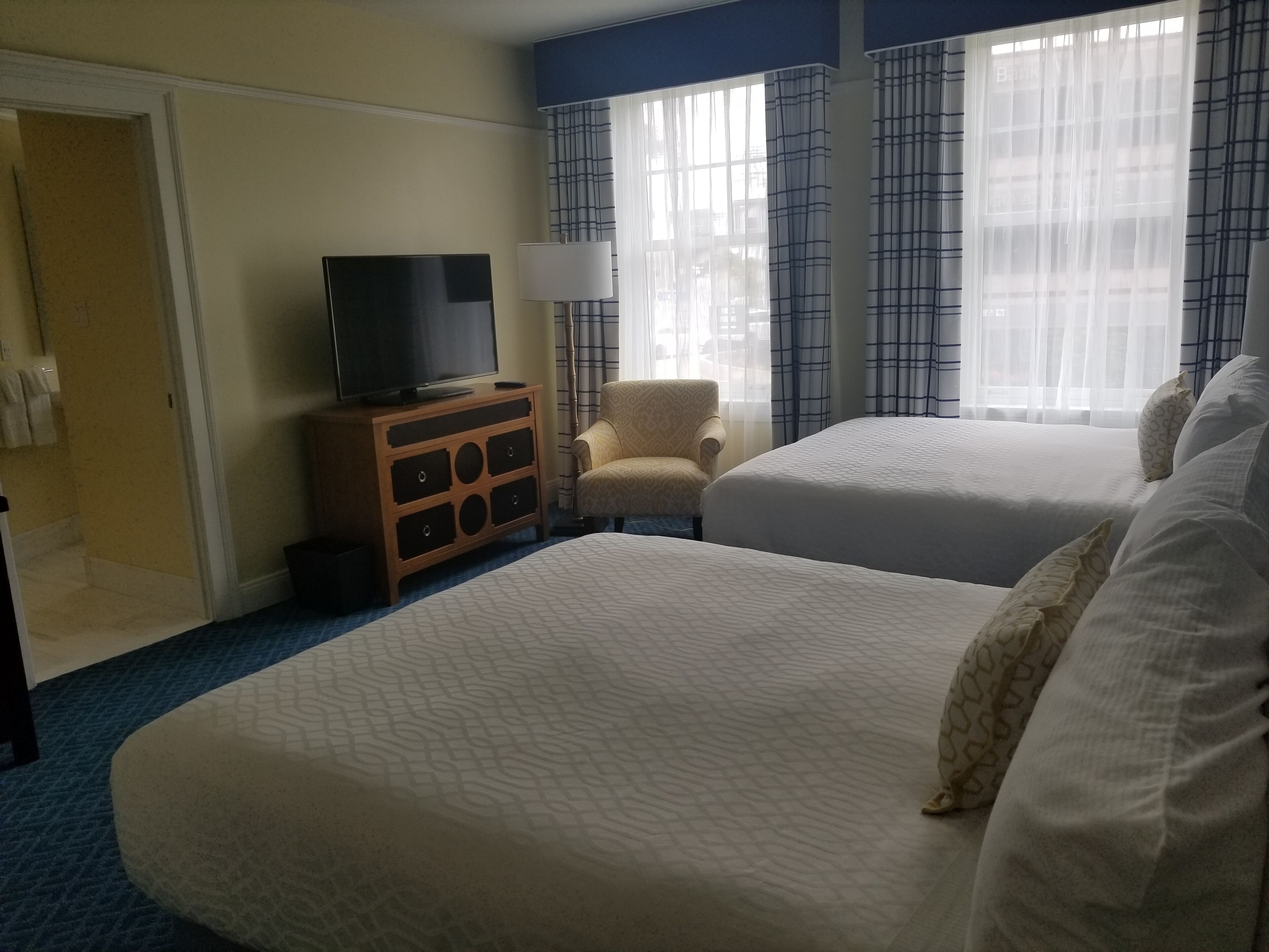 A hotel room with two beds, a television on a wooden cabinet, a chair, and a window with curtains.