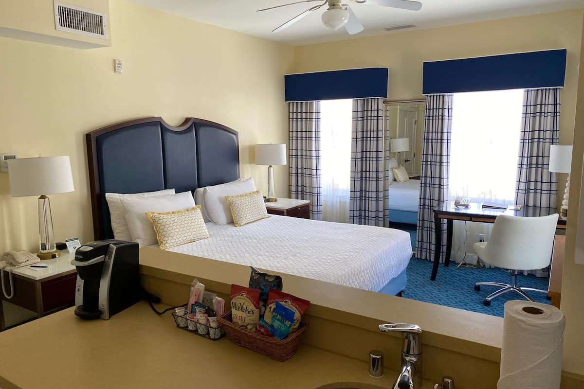 A hotel room with a large bed, a desk, a chair, a bathroom, and a view of the city.